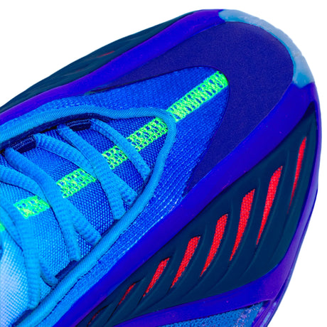Close-up of a blue athletic shoe showing the side panel with neon green knit accents and red detailing, photographed on a light gray background.